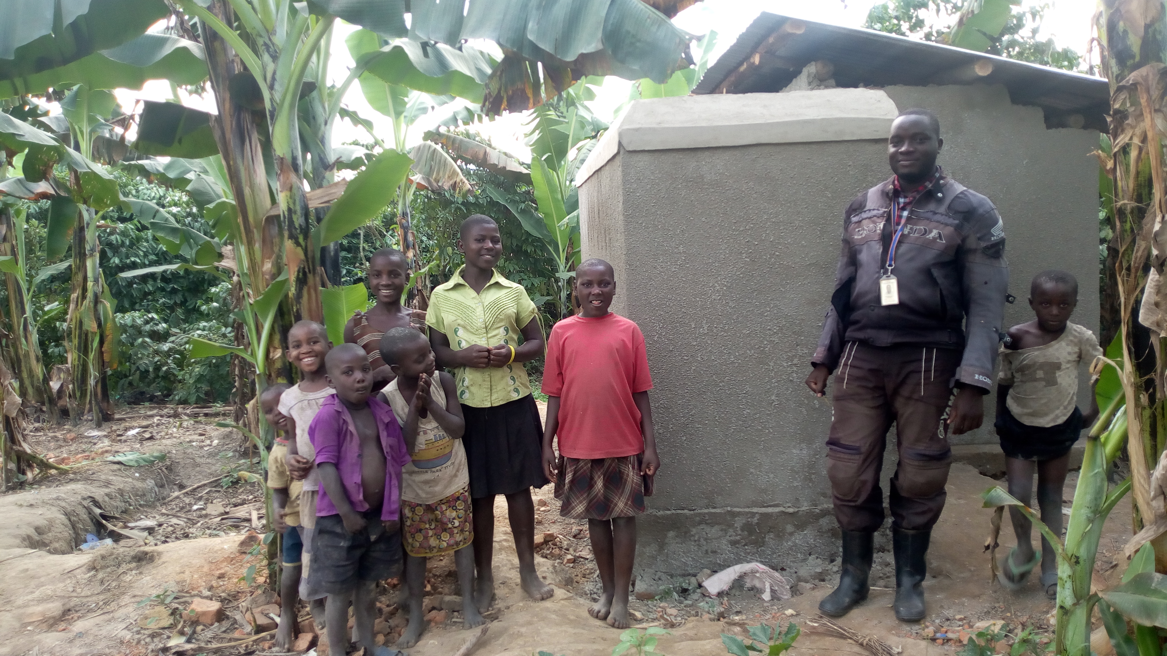 VisionFund staff, Denis, poses with children of Mariam Namutebi near their newly constructed latrine. The new laterine was constructed with a loan from VisionFund.
