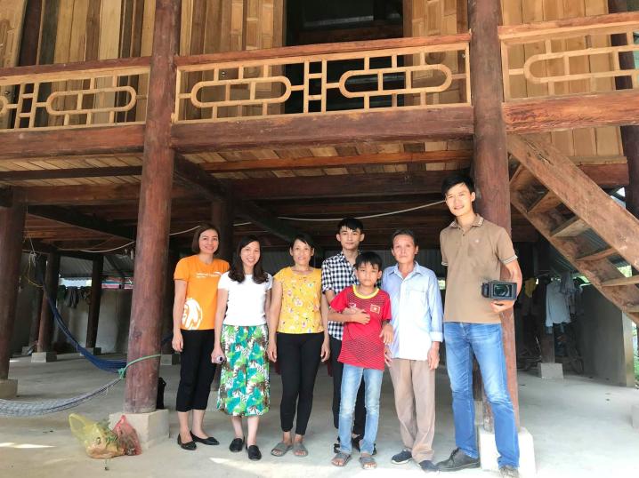 Ms. Than standing in front of her new home with World Vision staff