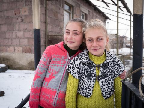 Two sisters standing outside in the snow in front of their home in Armenia