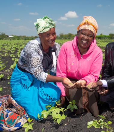 Two women in their field planting seeds with training from agricultural expert