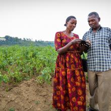 Husband and wife look at mobile phone while standing in farm in Rwanda